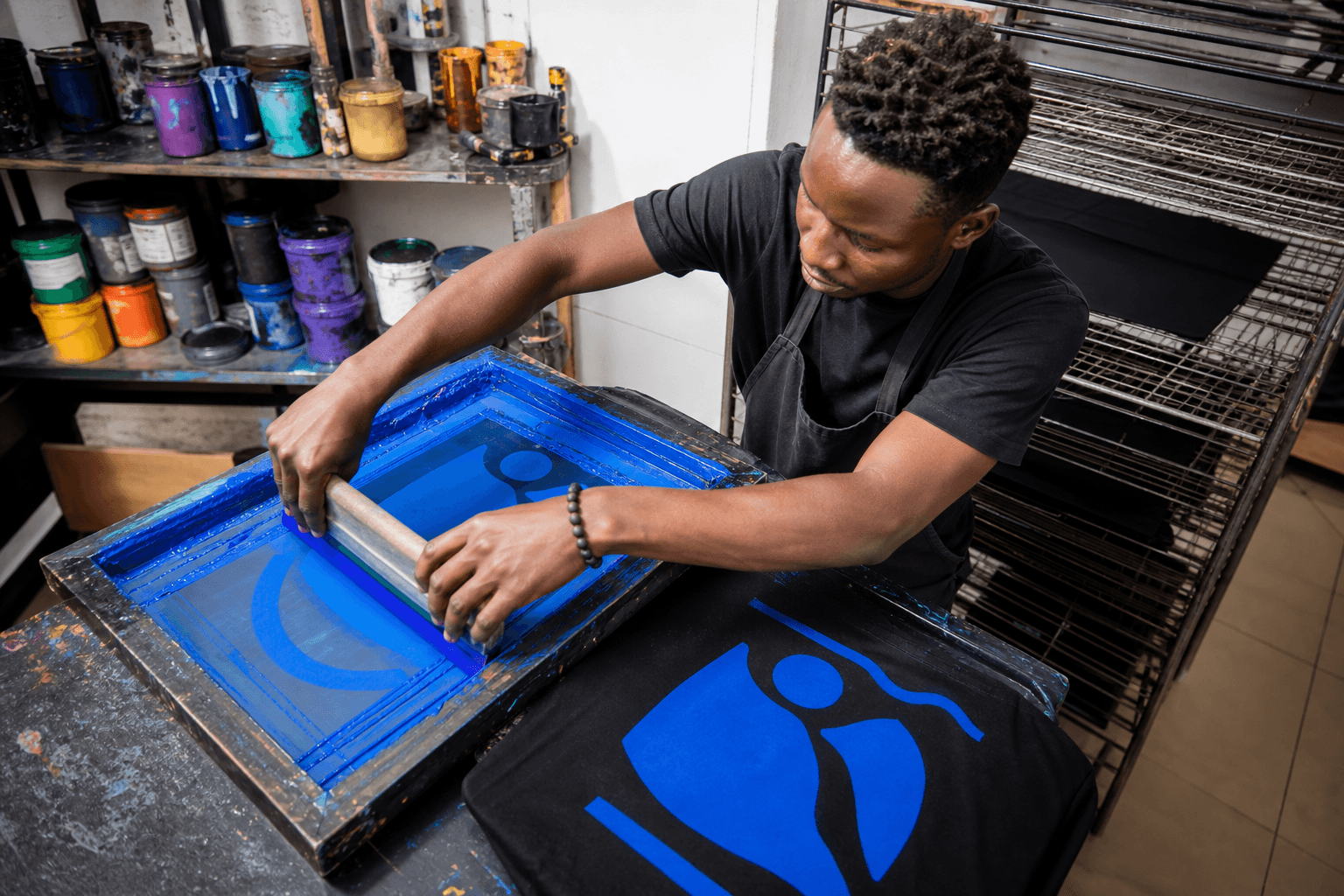 Demo craftsperson screen-printing a cobalt graphic onto a black T-shirt